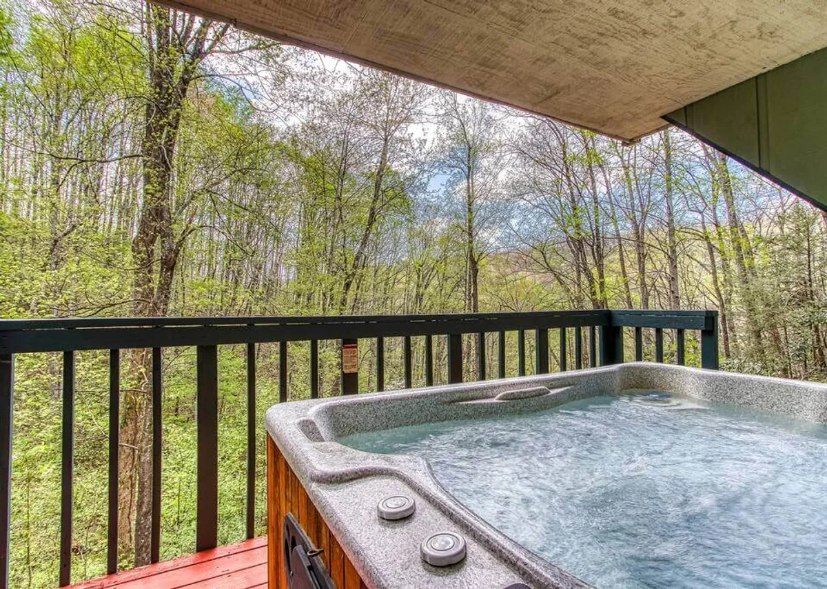 A view-focused image featuring a bubbling hot tub on a wooden deck with lush greenery beyond. The serene setting invites couples to unwind together while taking in the soothing sights and sounds of the Smokies.
