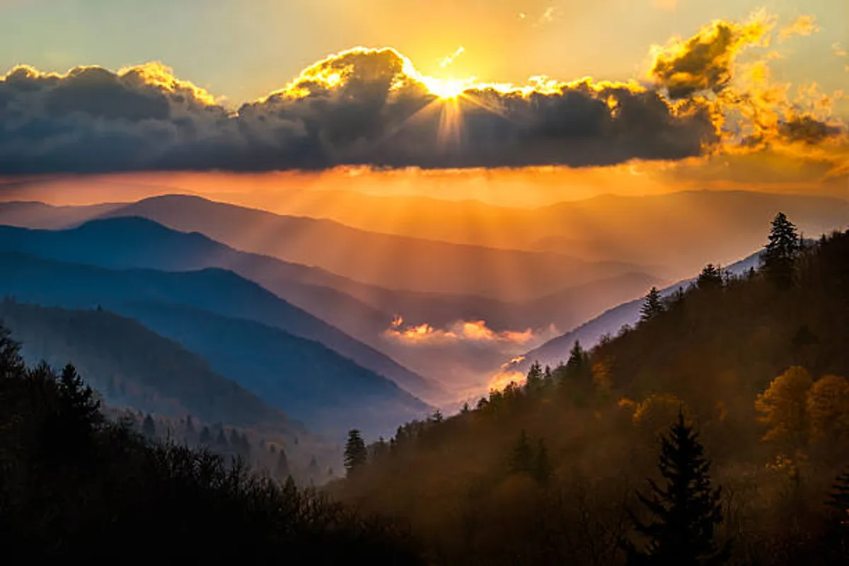 This image features a breathtaking sunset over the Smoky Mountains, with clouds bathed in warm light and blue mountain layers fading into the distance. It captures the awe-inspiring beauty and peaceful atmosphere that the locale offers.