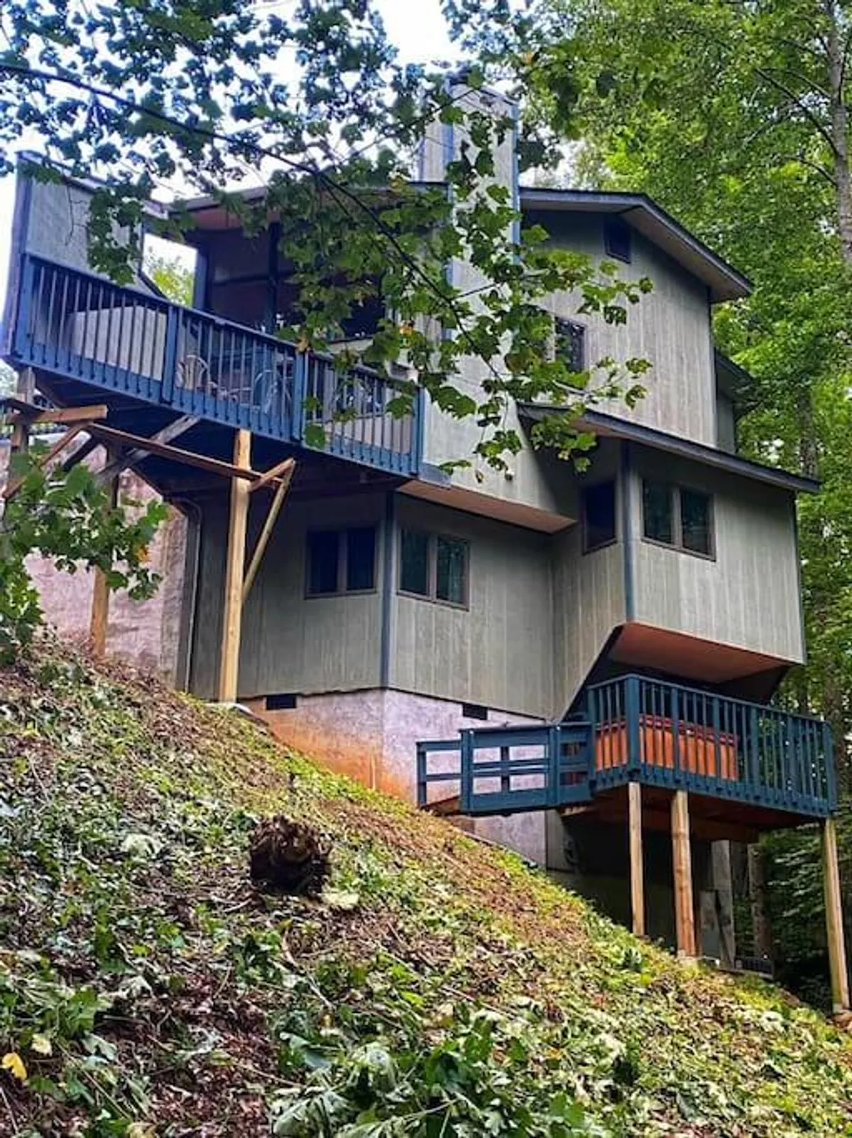 This image highlights the home's unique architectural design with expansive, elevated decks overlooking a lush, wooded landscape. The deck is framed by greenery, offering a secluded spot to relax, enjoy morning coffee, or gaze at the stars in the evening.