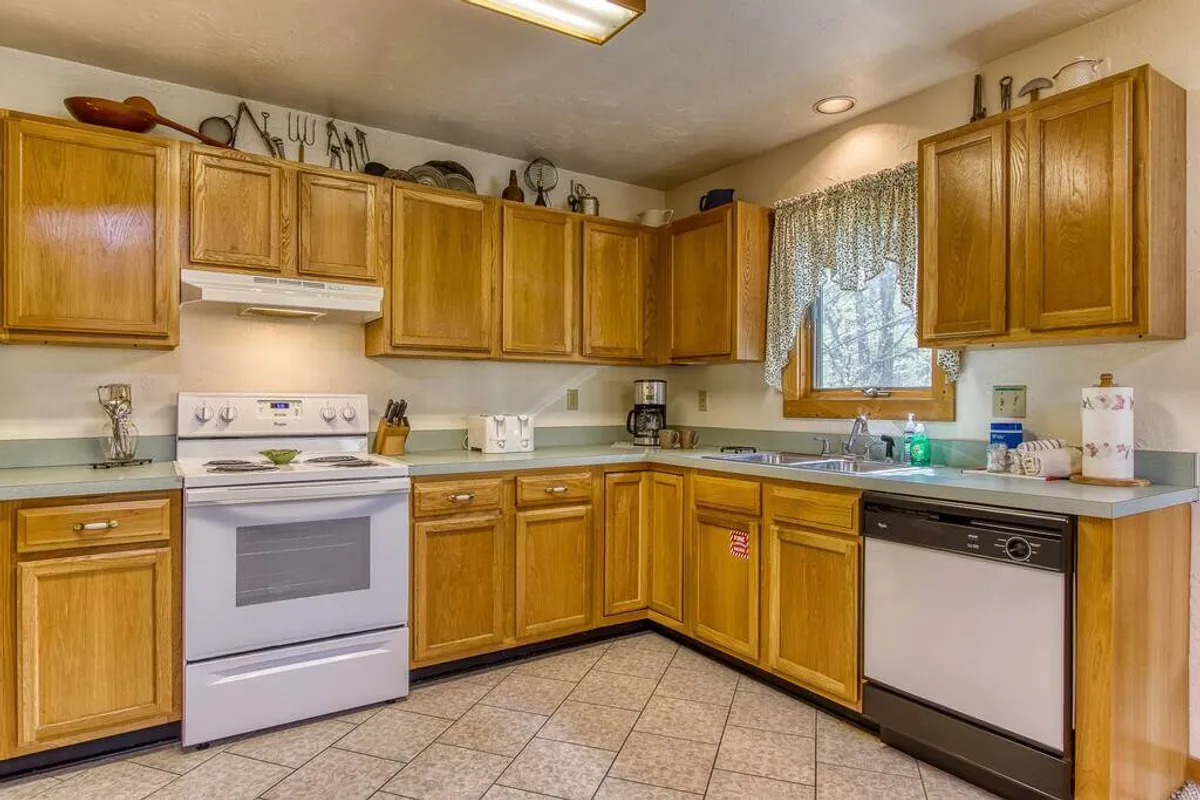 A cozy kitchen space with kitchen appliances, wooden cabinets, a kitchen window, a countertop, and a sink. The design is functional yet homey, set up for cooking, baking, and entertaining family or friends.
