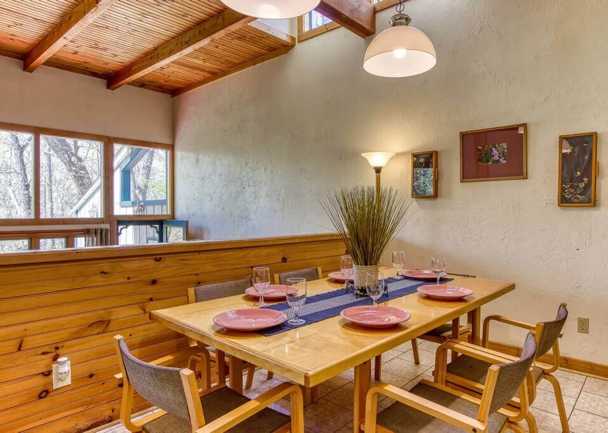 A beautifully set dining table with a decorative centerpiece, surrounded by windows that fill the space with natural light. The ambiance is warm and welcoming, ideal for family meals or gatherings with friends.