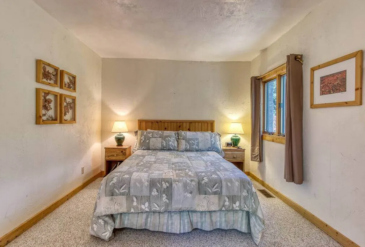 A serene bedroom featuring a comfortable bed with plush bedding, matching nightstands and lamps, a window flowing with natural light, and decorative artwork above the headboard. The overall ambiance is tranquil and inviting, ideal for relaxation and restful sleep.