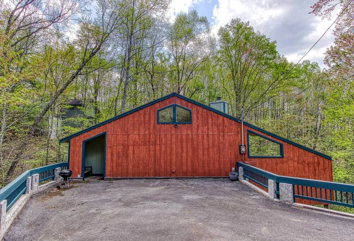 The inviting exterior of a private cabin, surrounded by trees with large windows and a paved driveway. The setting suggests a serene, secluded environment ideal for both family gatherings and quiet relaxation, showcasing the privacy and comfort of the property.