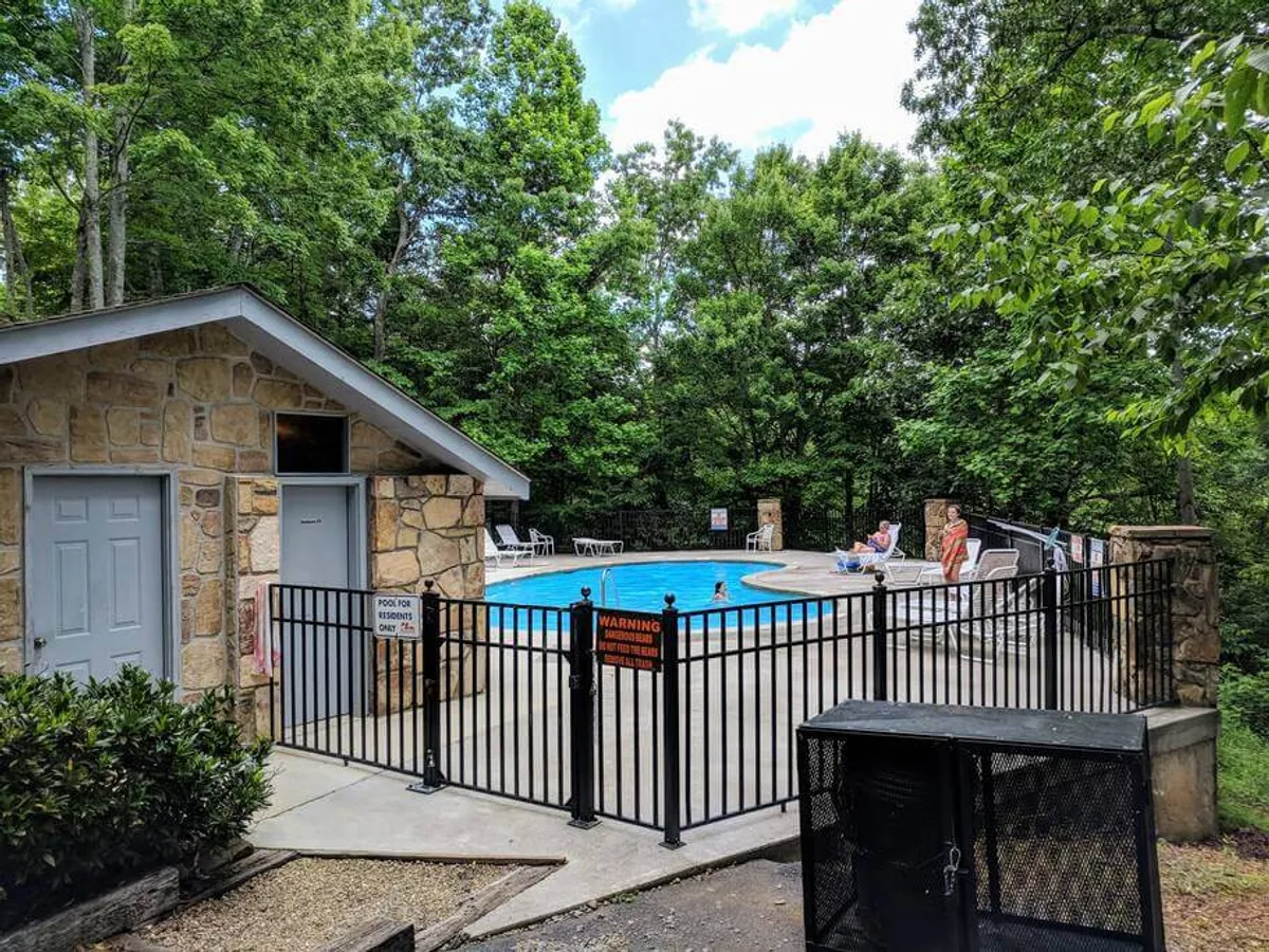 A sparkling swimming pool nestled among lush greenery, with poolside seating and a small building nearby. The inviting water, tranquil mood, and seating areas suggest relaxing swims, sunbathing, or quiet afternoons by the pool.